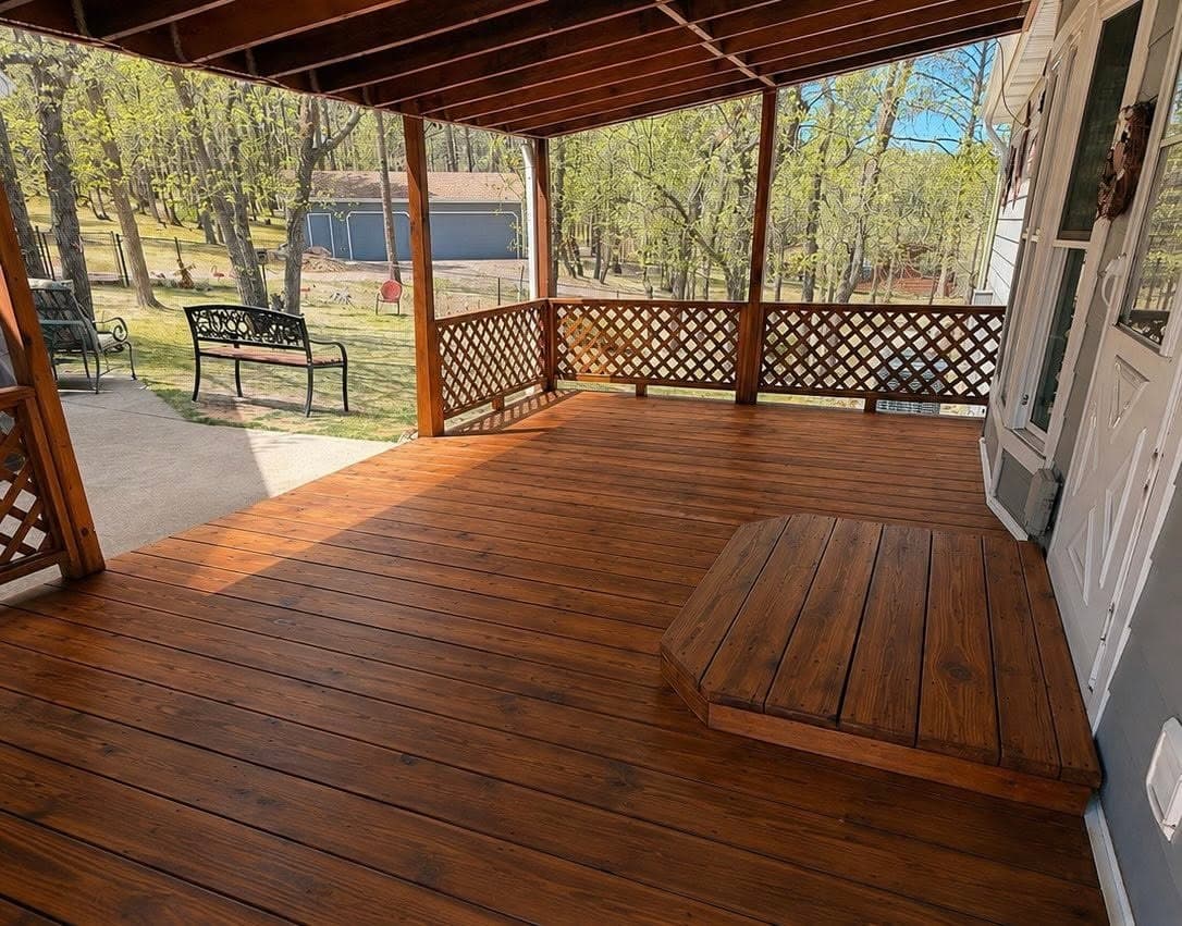 A covered porch deck stained a rich brown end to end, with a lattice rail and a bench beyond