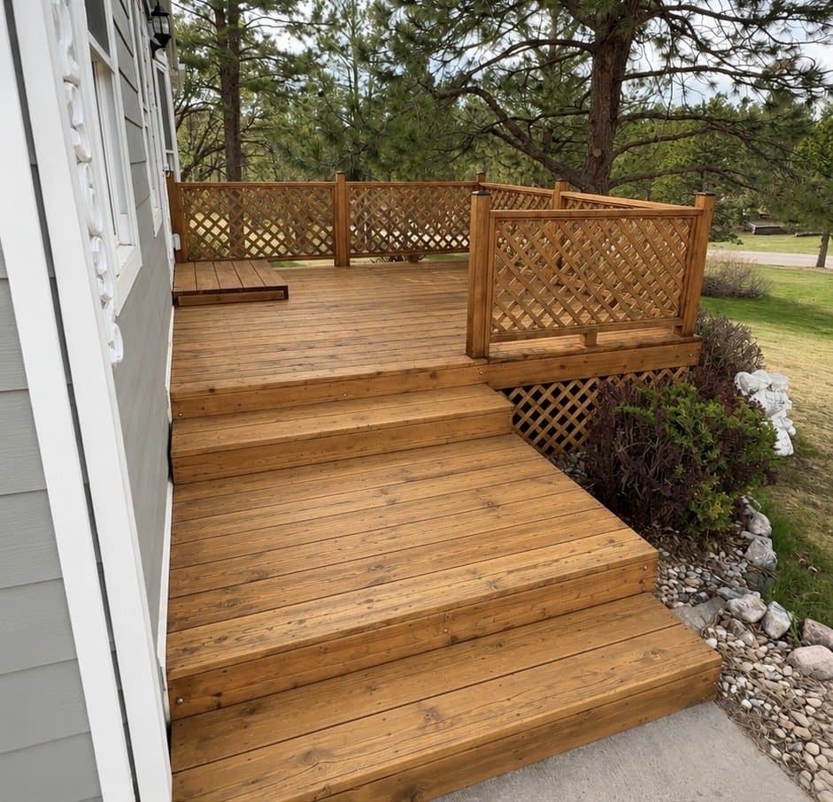 Deck with wide steps and a lattice privacy screen in a light natural cedar-tone stain, landscaping rock alongside