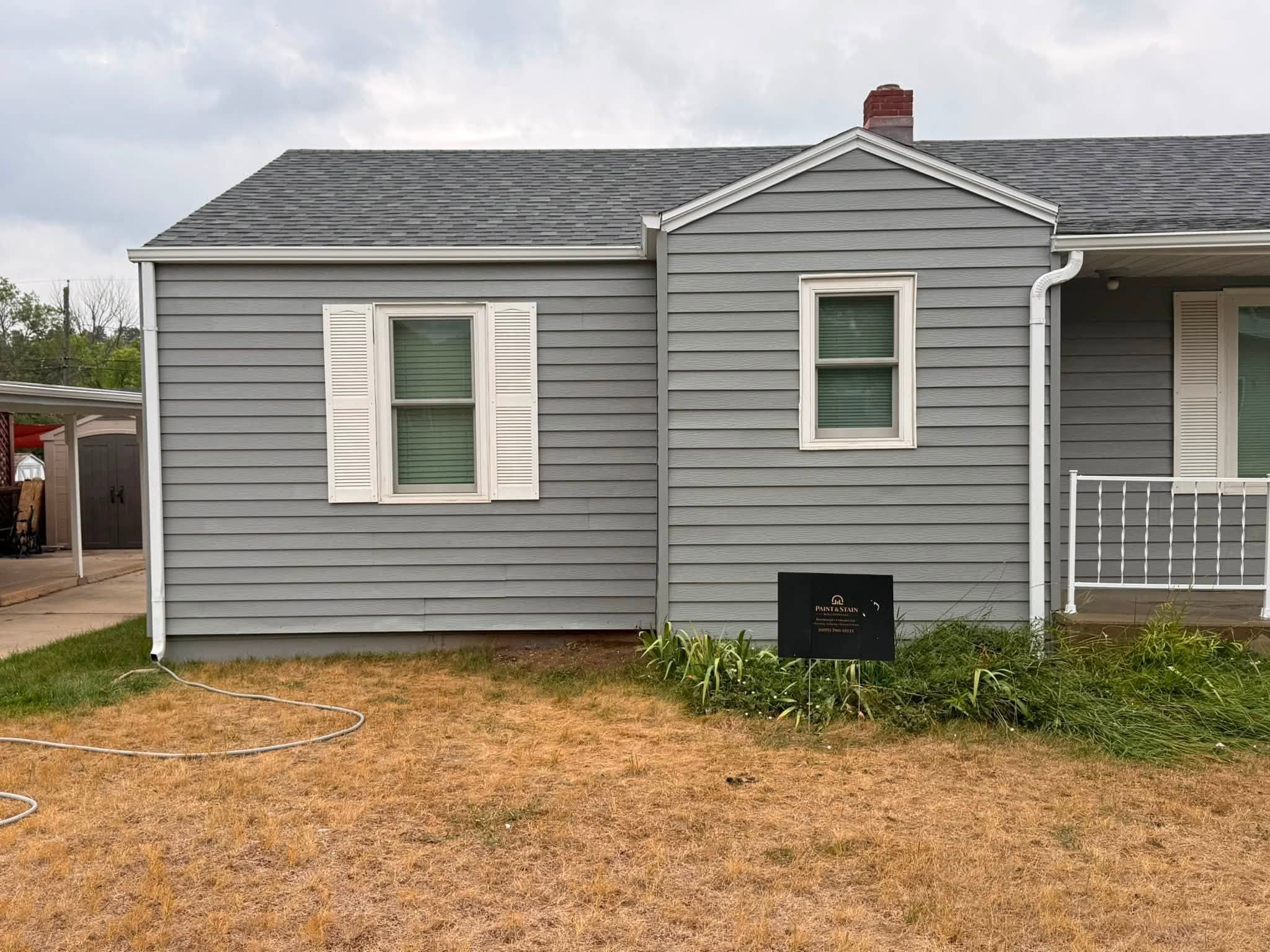 Finished front elevation of the same house in gray with white trim and cream shutters, with his own yard sign staked in the bed below
